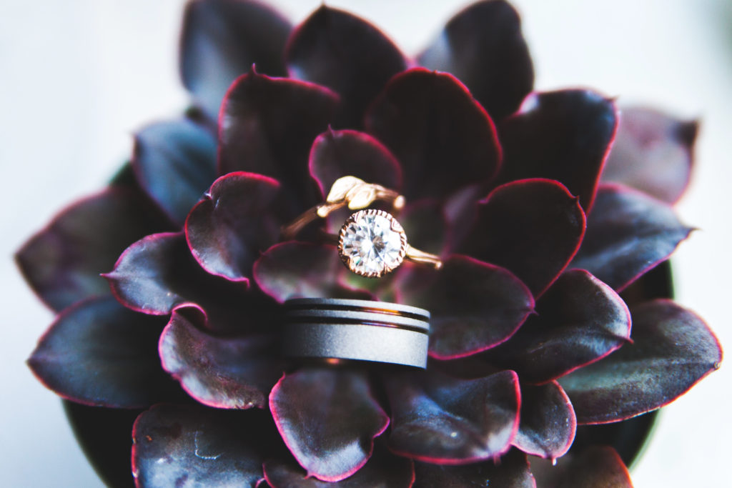 An engagement and wedding rings nestled in the center of a beautiful maroon flower.