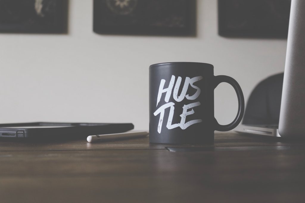 A black and white mug reading Hustle on a home office desktop.