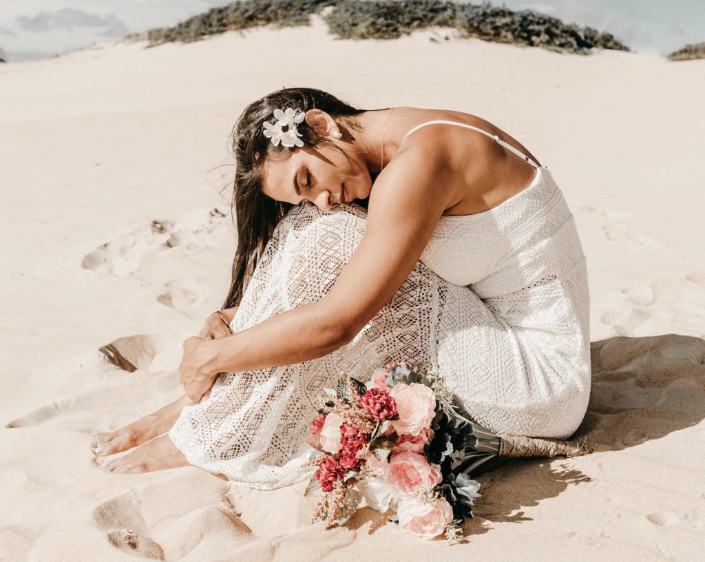 A beautiful boho bride posing thoughtfully on a beach.