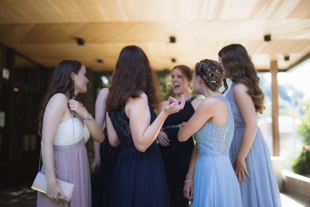 Women in formal dresses gather around a smiling new bride at her wedding reception.