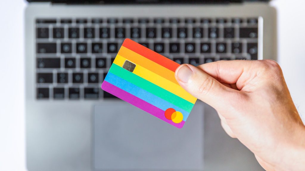 A fake credit card with rainbow stripes being held by an unseen person.