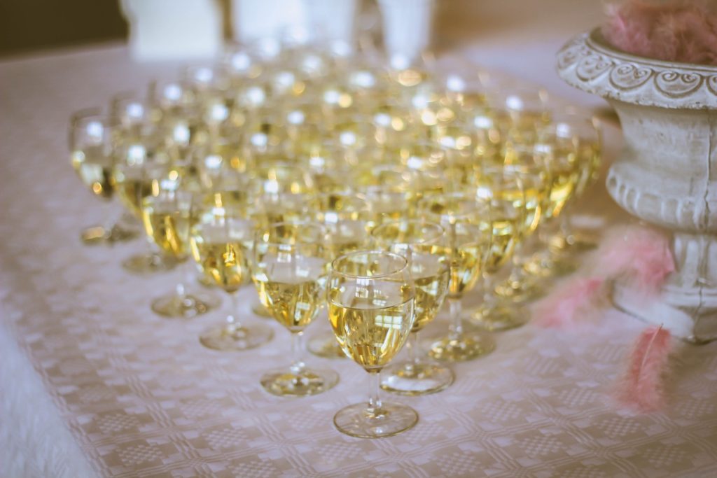 Several rows of wine or champagne in stemmed glasses set up on a table at a wedding reception.
