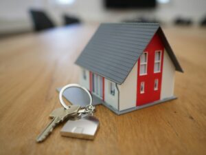 Miniature house keychain and a new house key on a conference table.