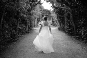 A bride walks through a clearing in the woods with her back to the viewer.