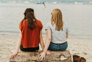 Two women on a rocky shoreline facing the water having a discussion