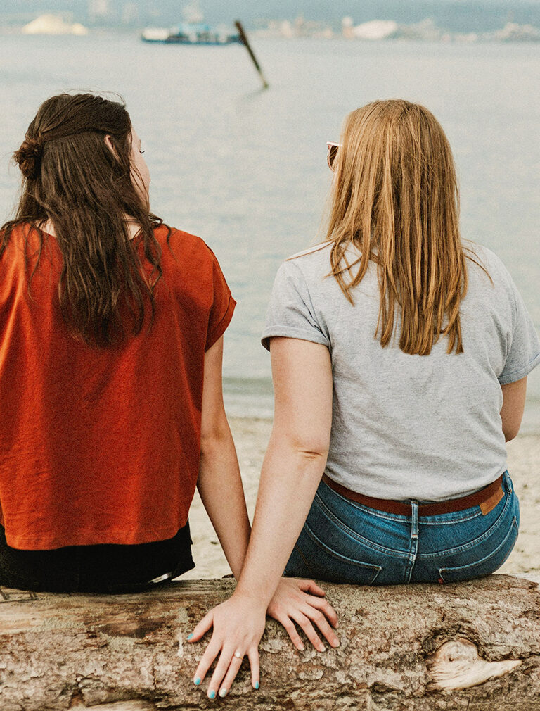 Two women on a rocky shoreline facing the water having a discussion