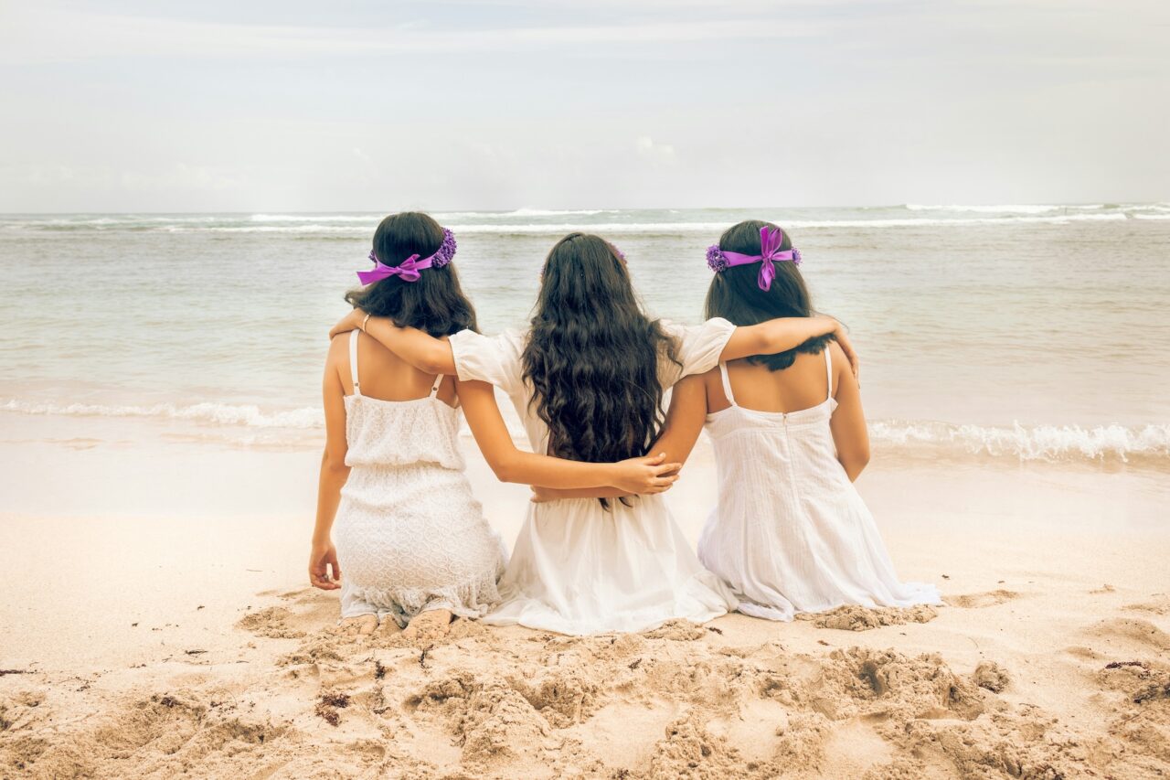 bride with maid of honor and bridesmaid on a beach with their backs turned to camera