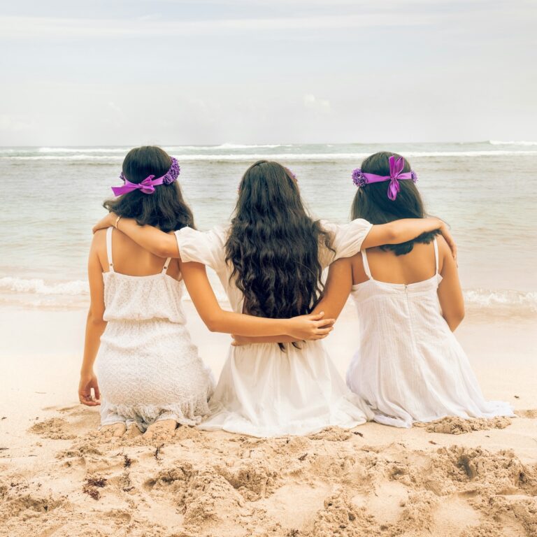 bride with maid of honor and bridesmaid on a beach with their backs turned to camera