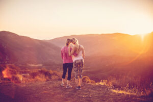 a mom and daughter in athletic clothes overlooking a valley during the sunset