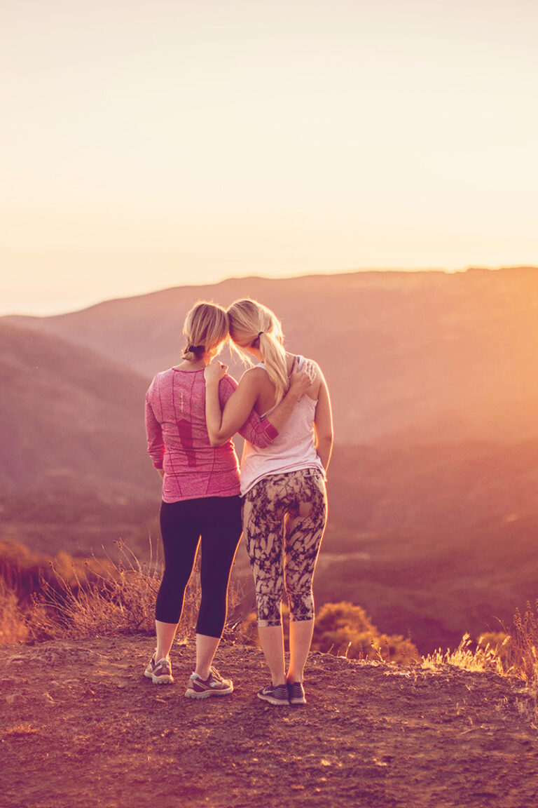 a mom and daughter in athletic clothes overlooking a valley during the sunset