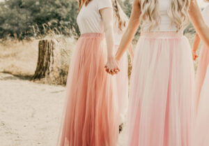 Bridesmaids in a circle holding hands wearing pink skirts near rustic woods