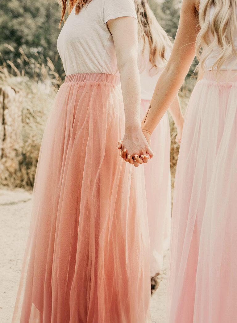 Bridesmaids in a circle holding hands wearing pink skirts near rustic woods