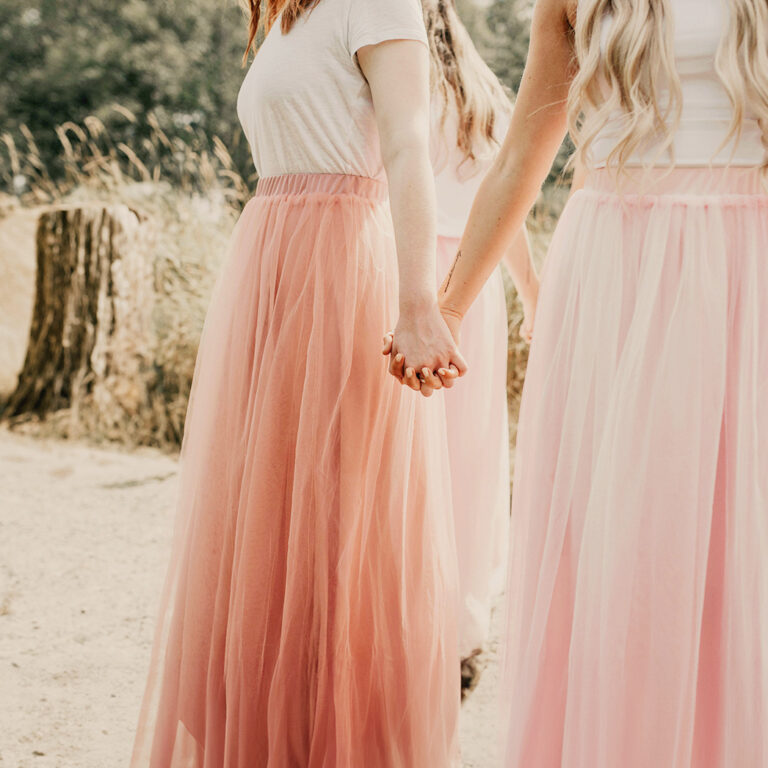 Bridesmaids in a circle holding hands wearing pink skirts near rustic woods