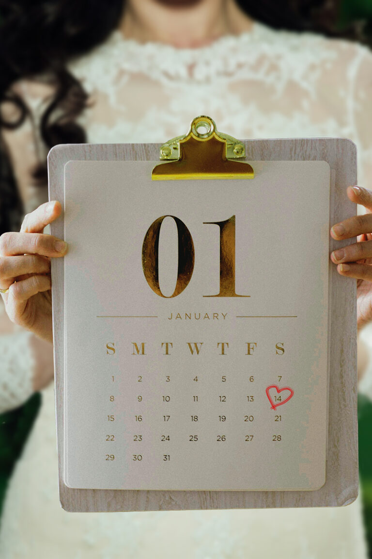 bride wearing a wedding gown in background, holding a calendar on a clipboard in foreground with her wedding date circled in a red heart