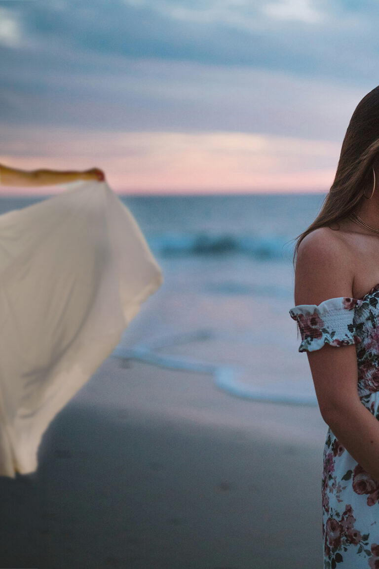 pregnant bridesmaid on a beach while bride poses in gown behind her during sunset