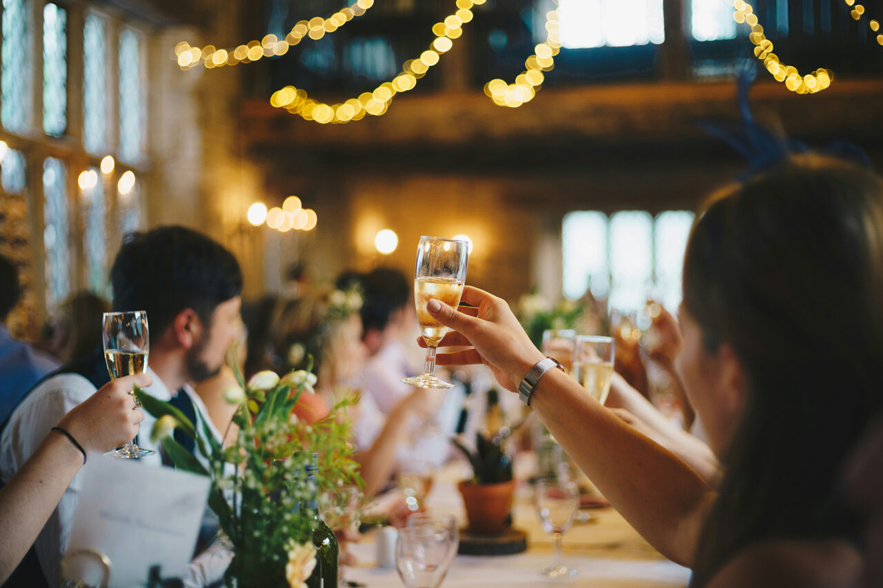 guests toasting at a wedding with string lights blurred in the background