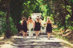 a bride and bridesmaids walking away down a sunny dappled tree-lined street