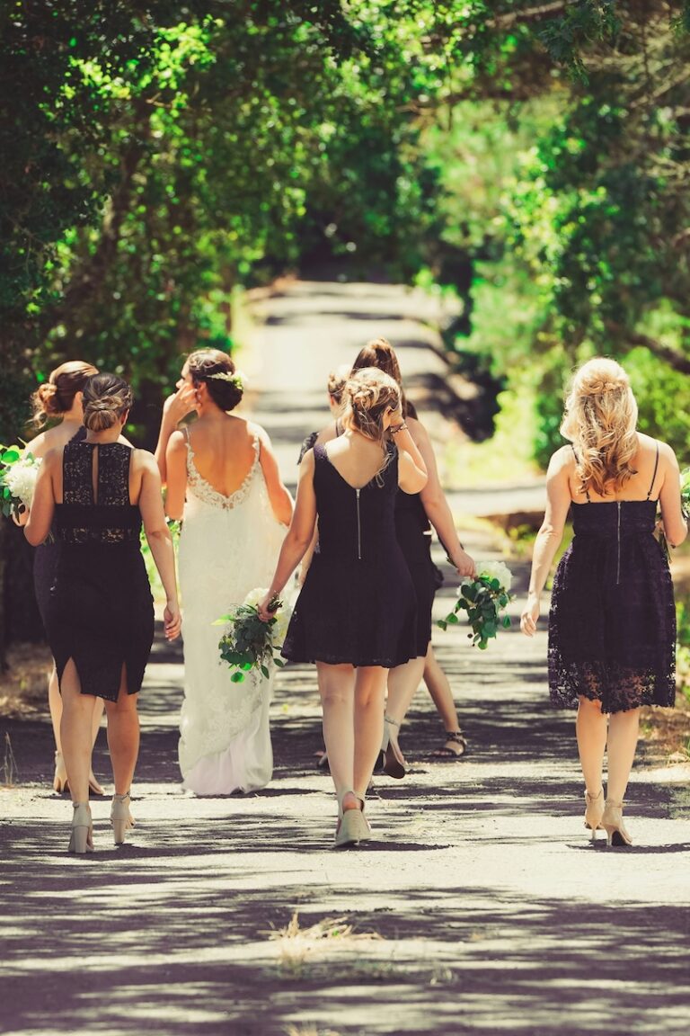 a bride and bridesmaids walking away down a sunny dappled tree-lined street