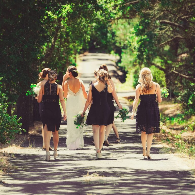 a bride and bridesmaids walking away down a sunny dappled tree-lined street