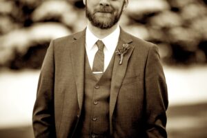 close up shot of a groom standing in front of snow covered trees, face cropped