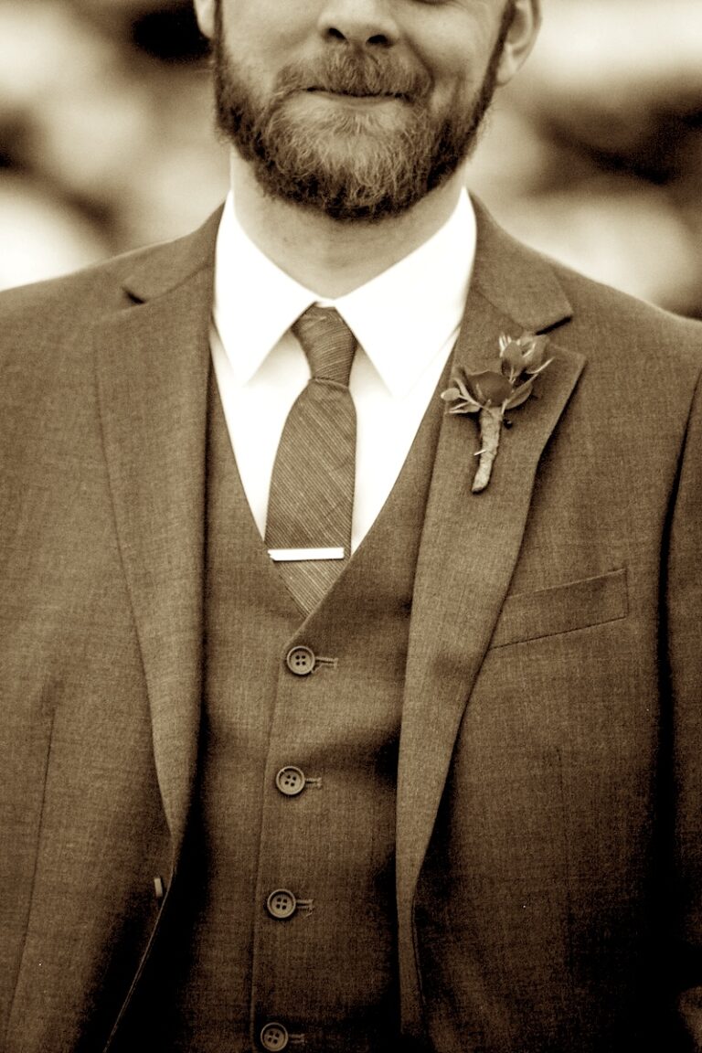 close up shot of a groom standing in front of snow covered trees, face cropped