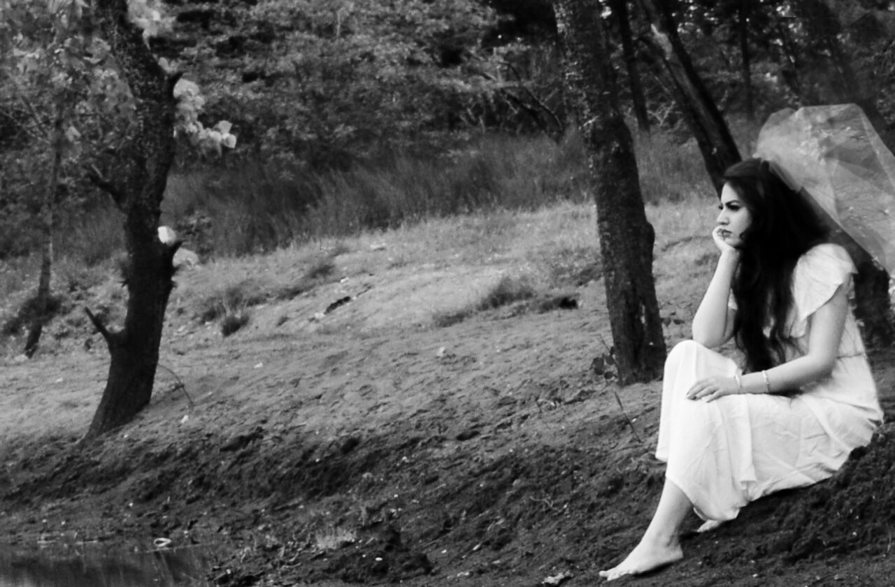 sad bride sitting on riverbank barefoot