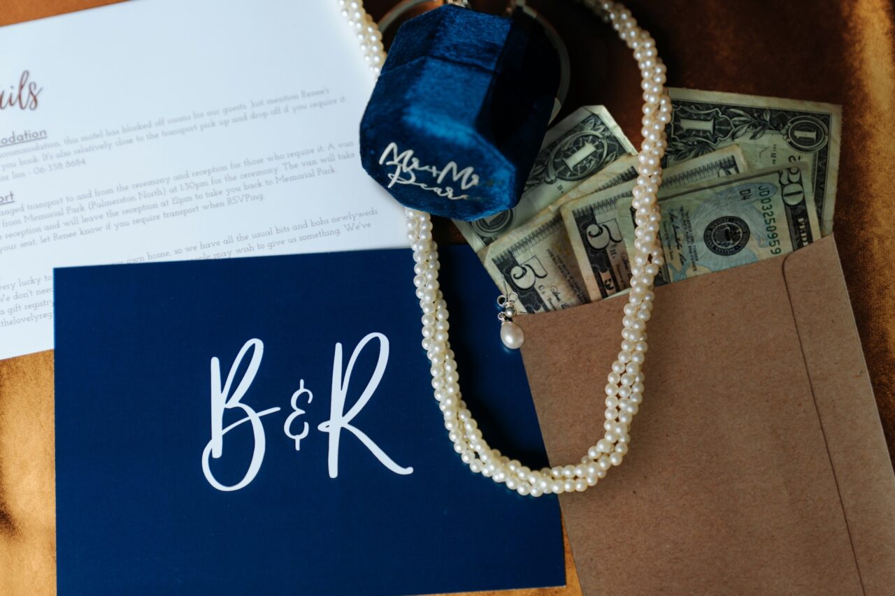 a brown craft paper envelope filled with cash on a table with pearls, wedding rings, and invitations