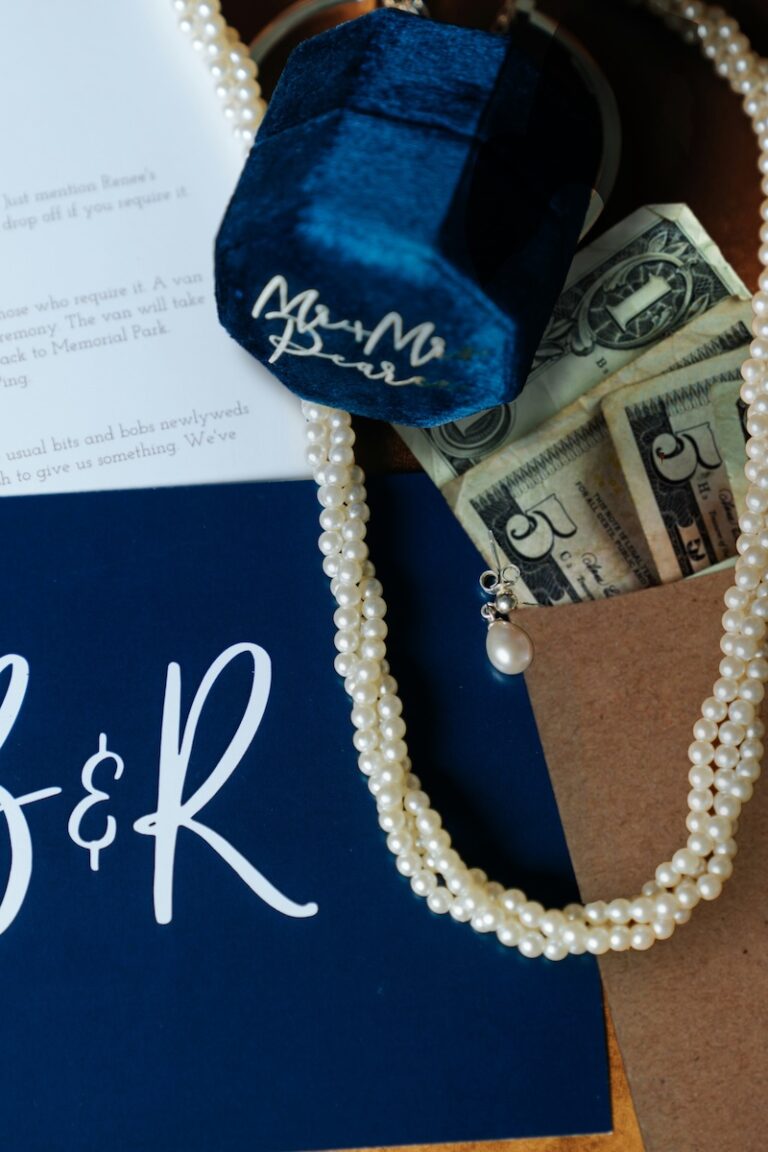 a brown craft paper envelope filled with cash on a table with pearls, wedding rings, and invitations