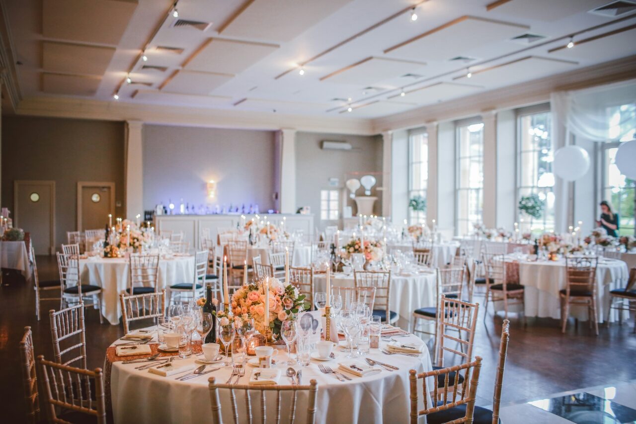 beautiful reception hall decked out with flowers and pink tableclothes, and gold cane chairs, ready for guests