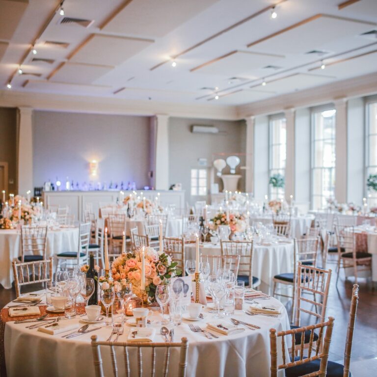 beautiful reception hall decked out with flowers and pink tableclothes, and gold cane chairs, ready for guests