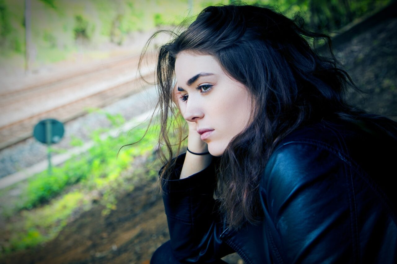 Thoughtful brunette woman looking at railroad tracks from window